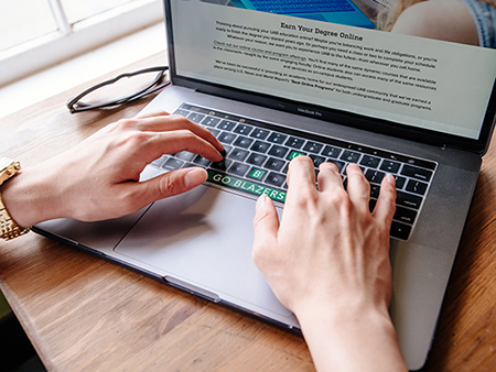 Shot from above, woman's hands are typing on a laptop computer on wooden table in Church Street Coffee & Books, 2019.