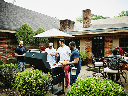 Laughing group of friends and family barbecuing in backyard before party on summer afternoon