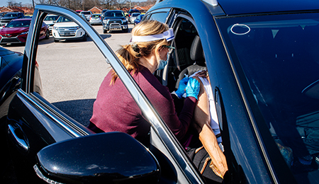 Overall of people standing in line near white tents at the UAB COVID-19 Vaccination Site at Parker High School on February 10, 2021. 