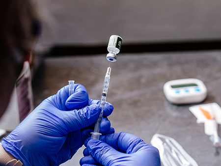 Close-up, hands wearing blue PPE (Personal Protective Equipment) gloves are filling a syring with a dose of the Pfizer COVID-19 (Coronavirus Disease) vaccine on January 15, 2021.