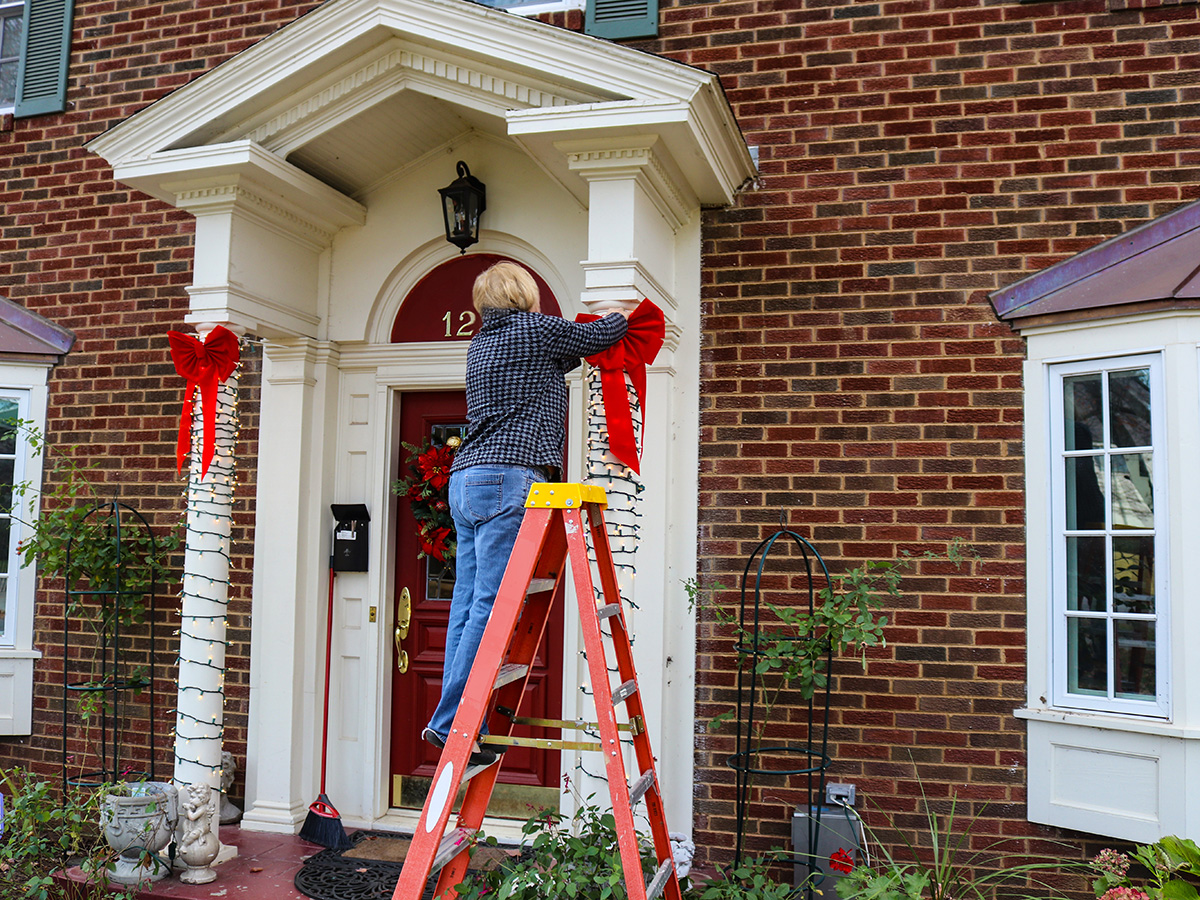 Person on a ladder putting holiday decor on the exterior of the house