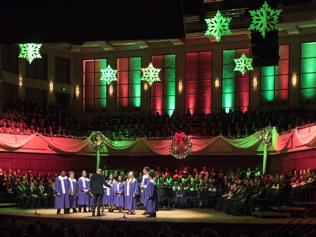 Group of students on stage lit with green and red lights in purple gowns