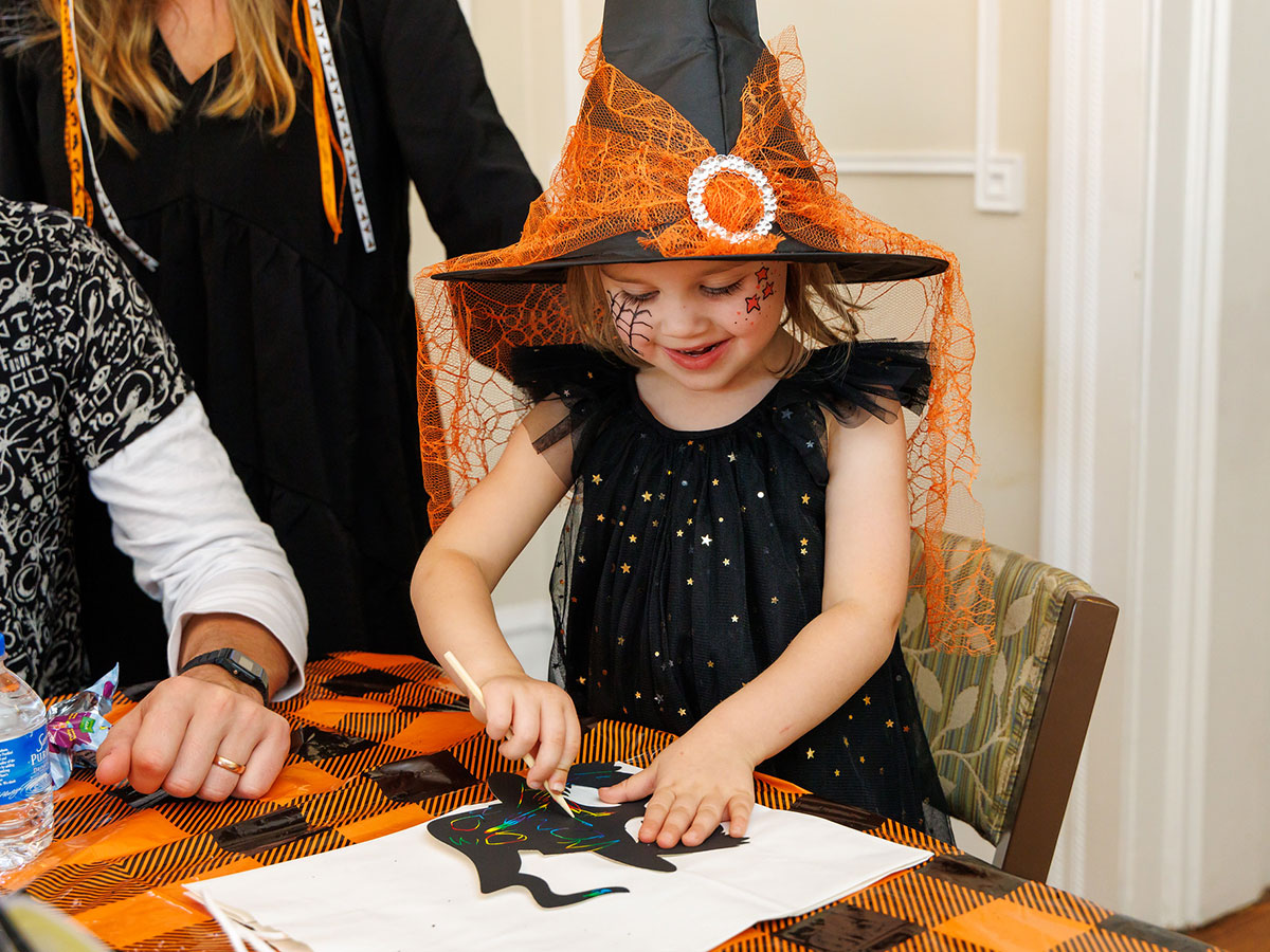 A young girl in a witch hat creating halloween-themed arts and crafts.