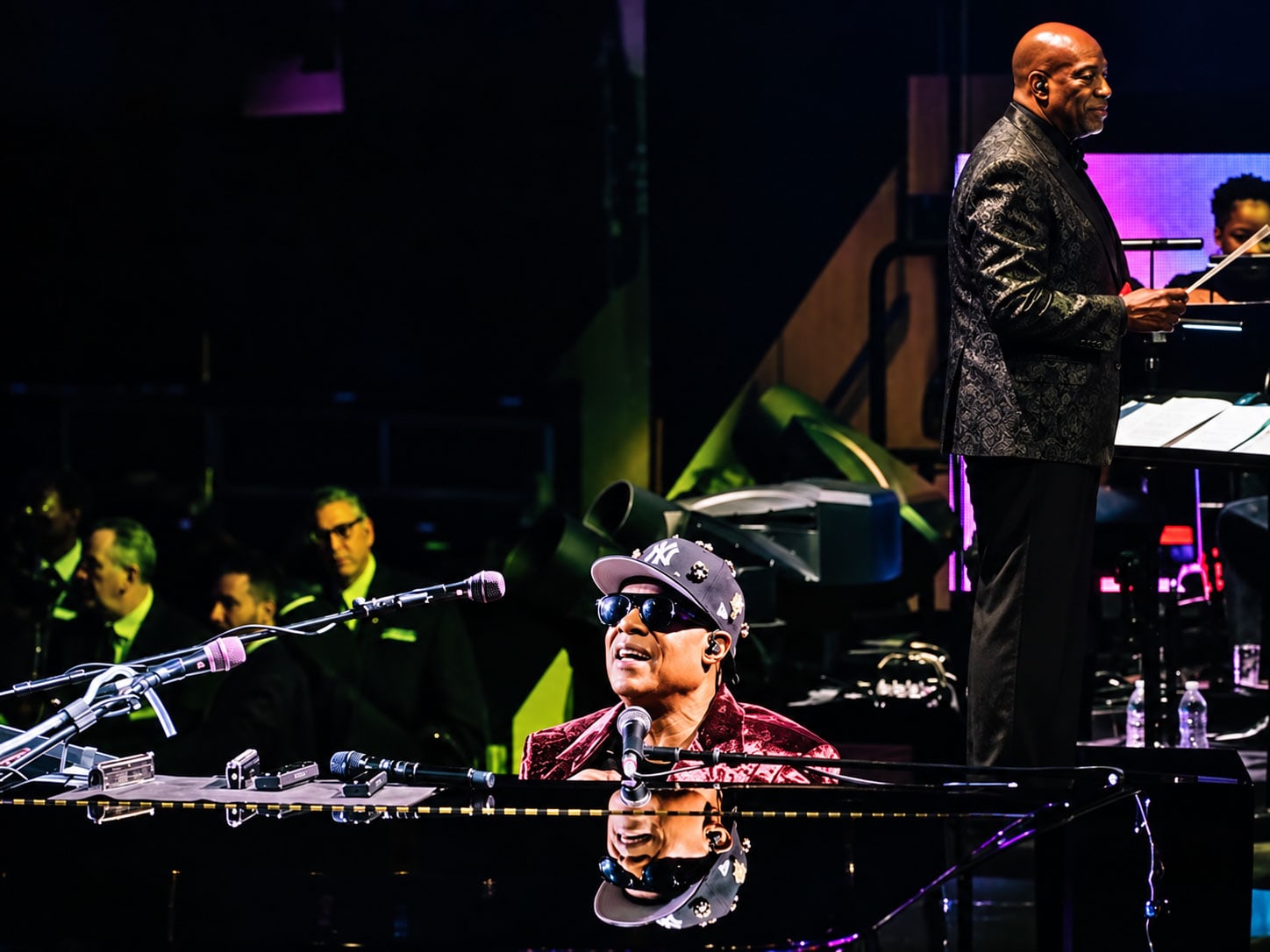 A man plays piano on stage, as another man stands and conducts the band.