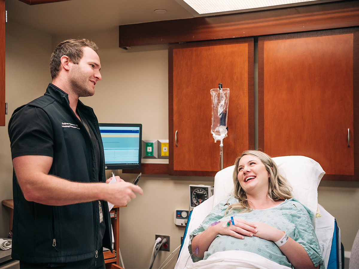 An anesthesiologist is talking with an expectant mother lying in a hospital bed in a pre-op room prior to her baby's birth.
