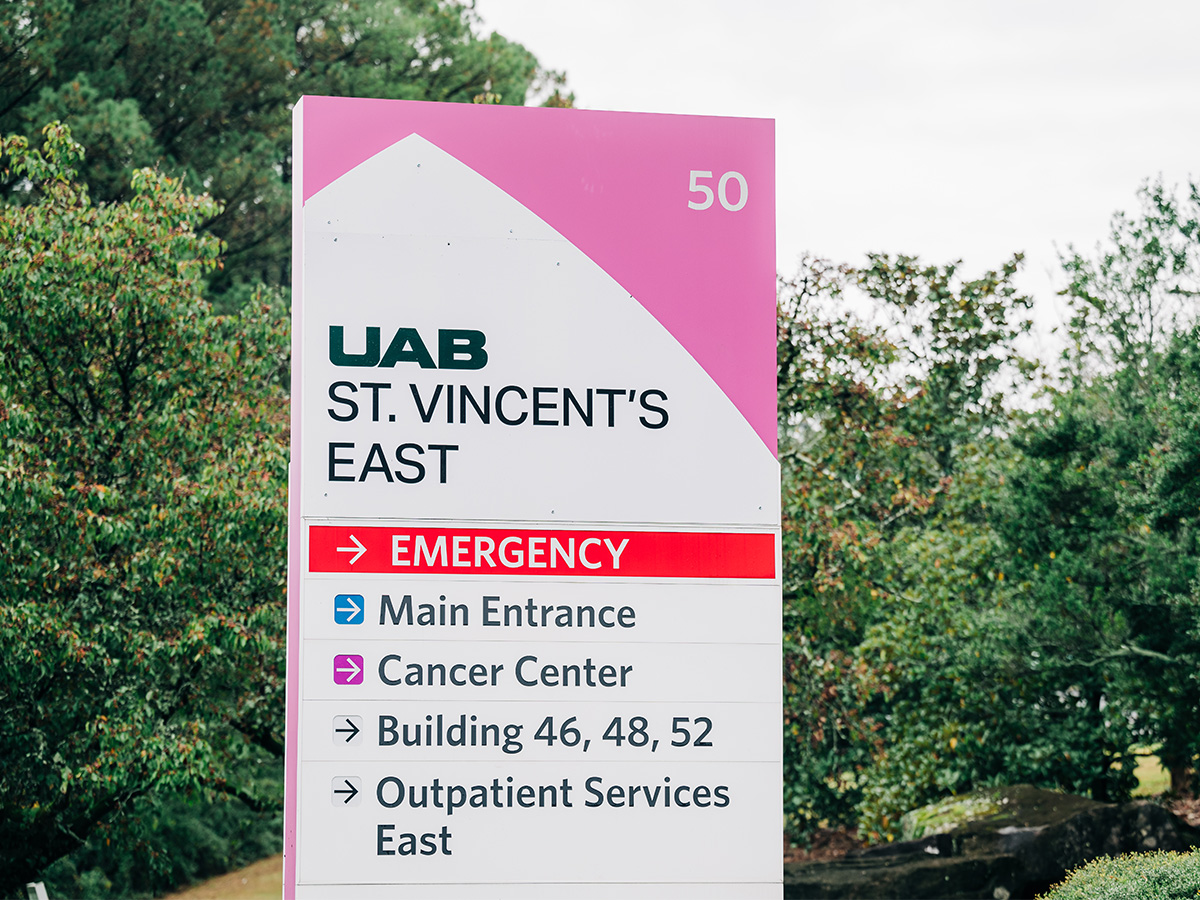 Close-up of roadside signage that reads "UAB St. Vincent's East" with small trees in background, November 1, 2024