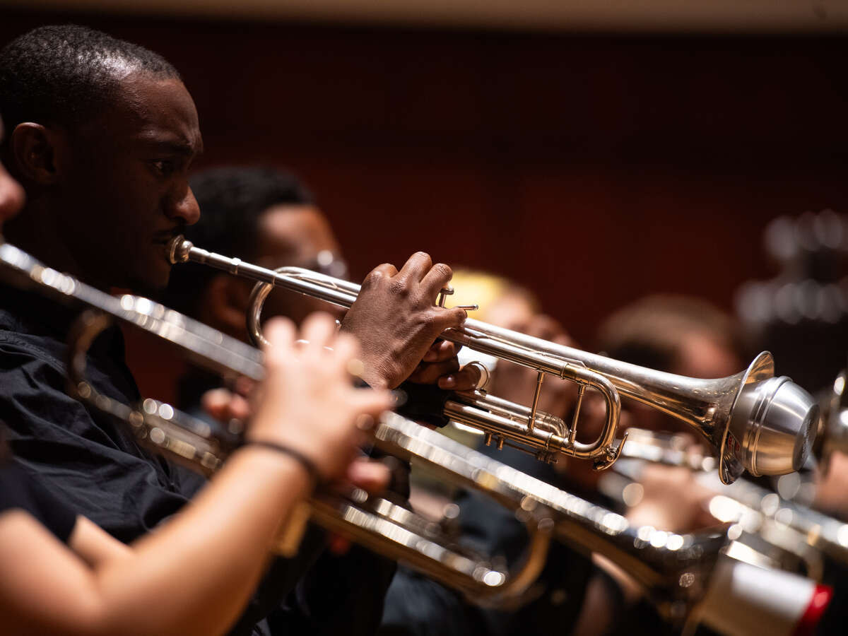 Close-up of students performing their musical instruments in rehearsal, ranging from trumpet and trombone to marimba. 