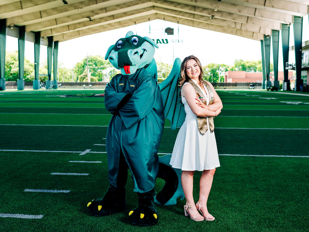 Anna Grace poses with Blaze, who is in a graduation gown, on the UAB football practice field.