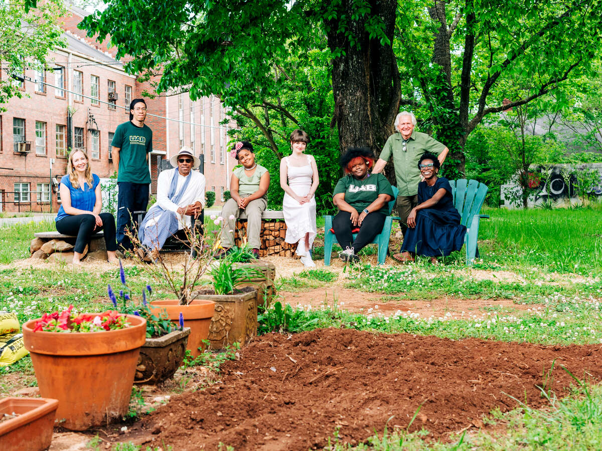 People including a child and elders relax in chairs and on benches outside in a garden space.