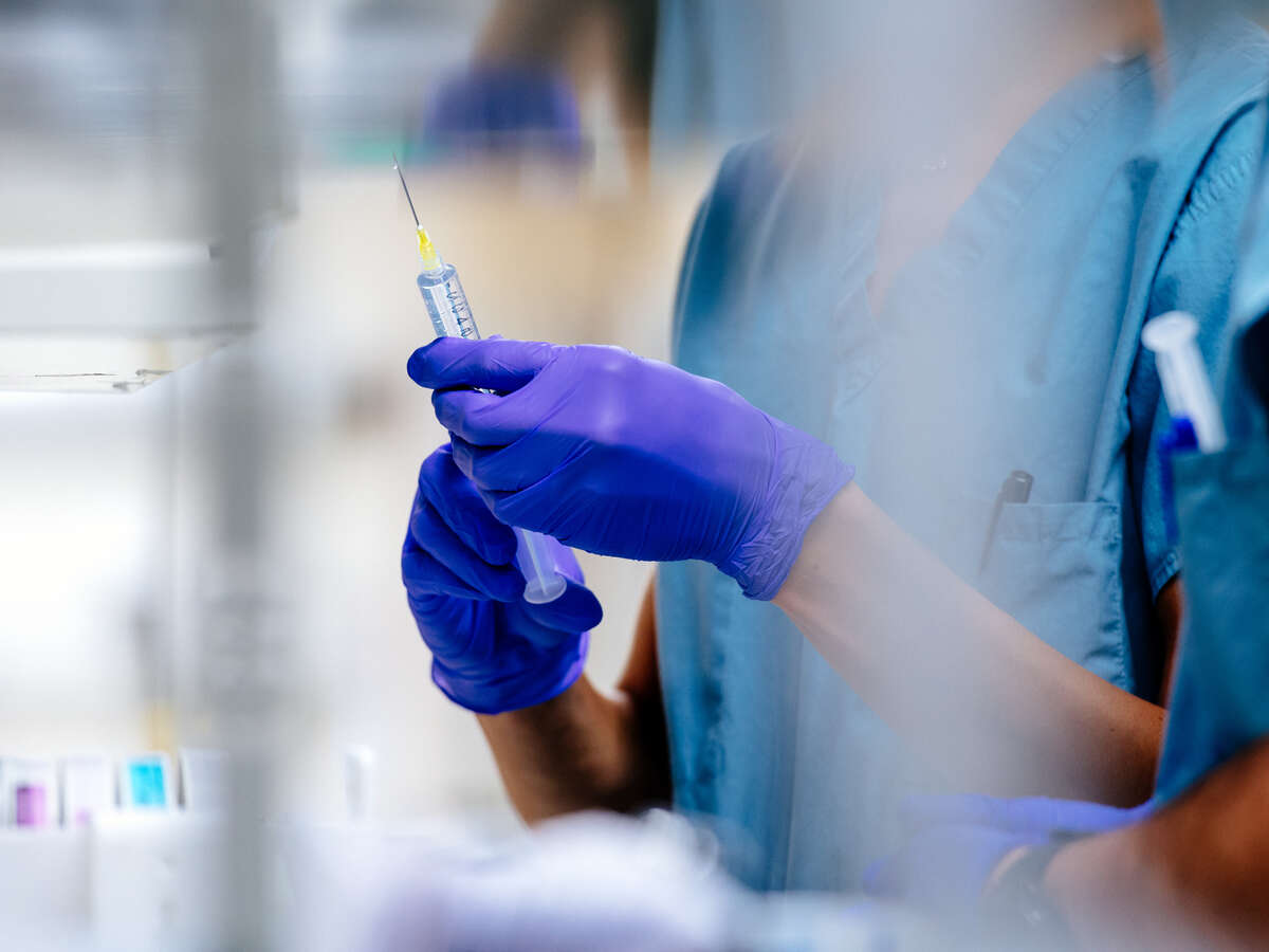 Close-up, gloved hands while using a syringe. 
