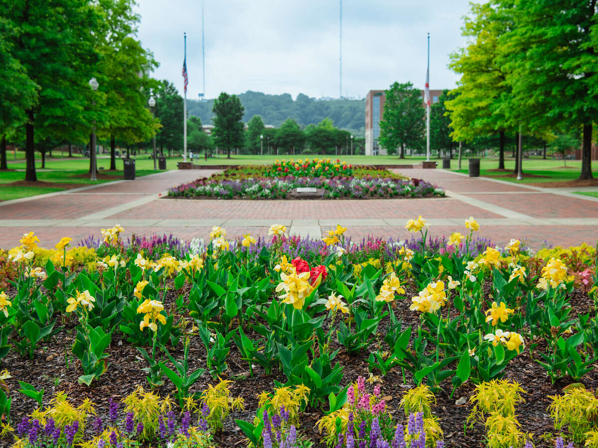 Large ornamental flower bed located in a large brick paved area with the United States Flag and the Alabama State flag on flagpoles under an overcast sky.