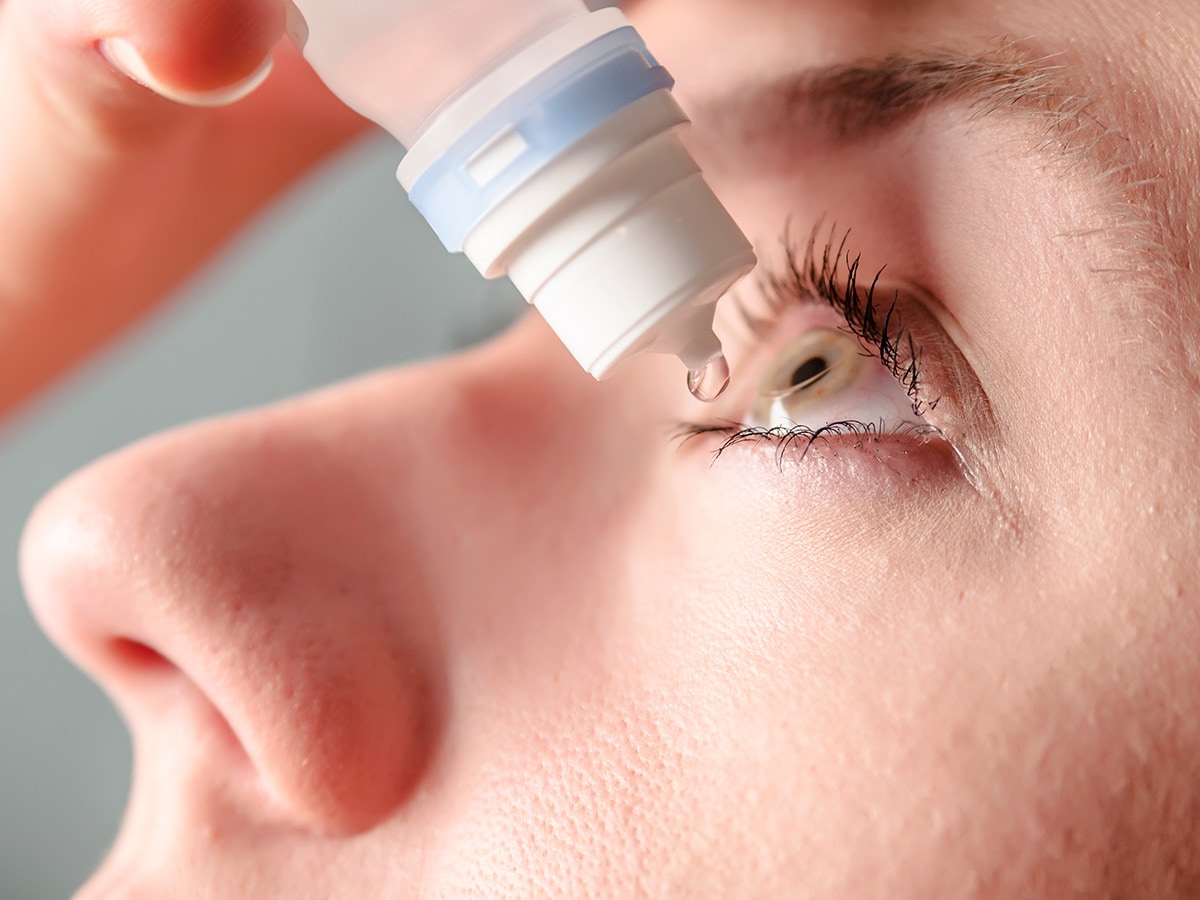 Close up view of young woman applying eye drop to left eye.