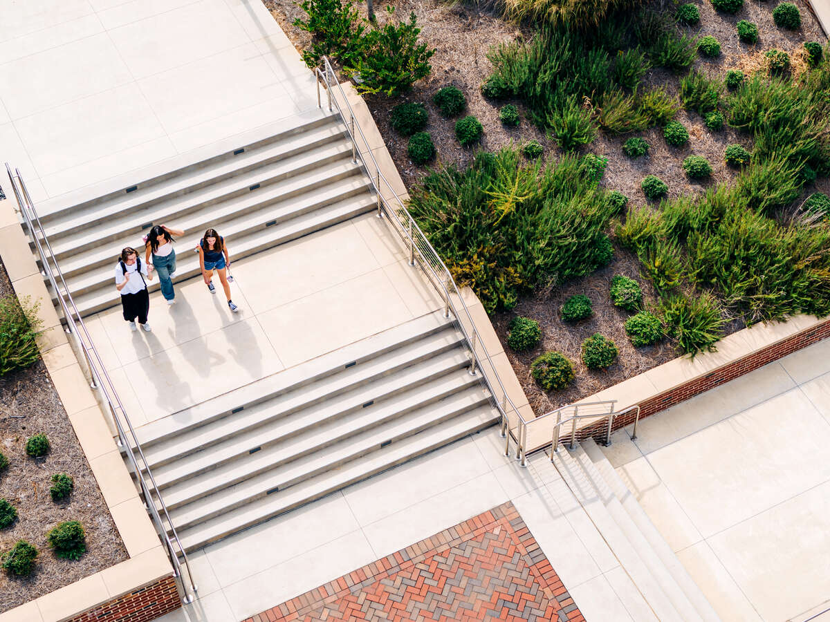 Shot from above, drone photo of students wearing backpacks and walking on exterior stairs of Sterne Plaza