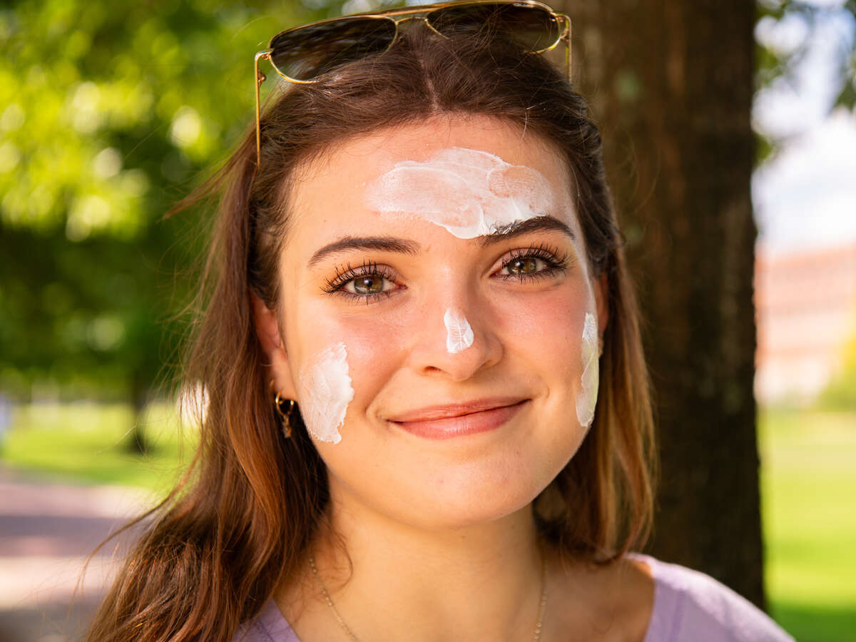 Close-up of smiling woman with sunscreen lotion visible on her forehead, cheeks, and nose before application.