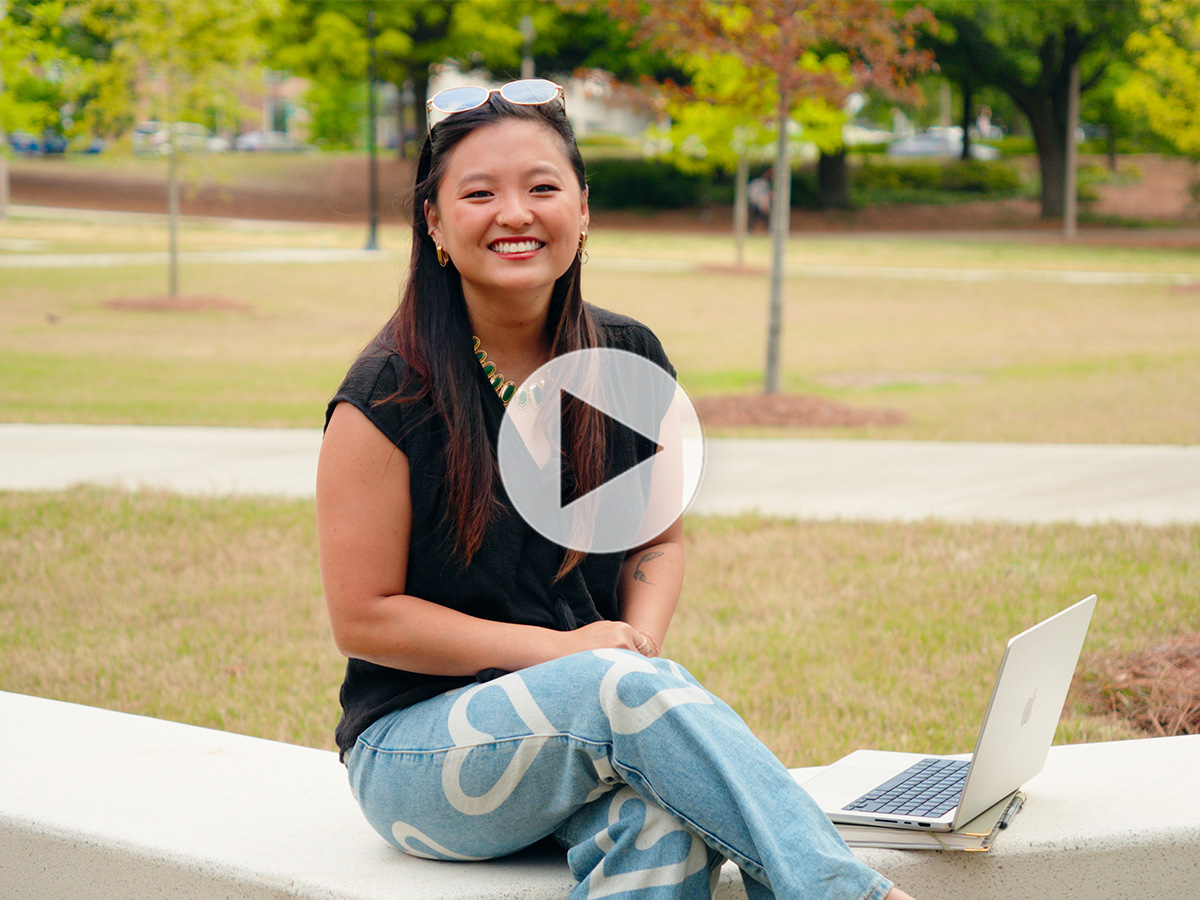  Photo of Chanah Fallin sitting outside on campus with her laptop and notebook.