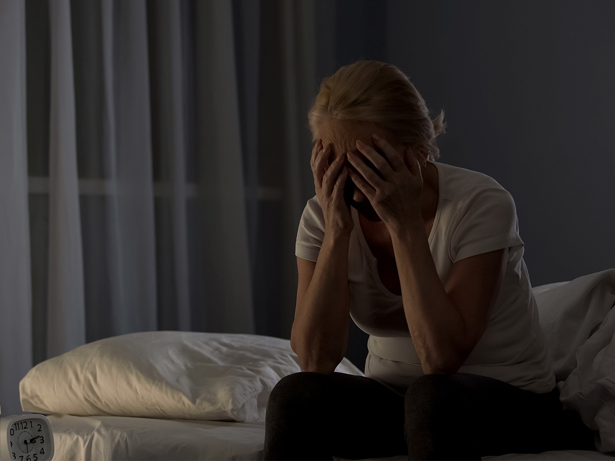 Lady sitting on bed night, covering face with hands