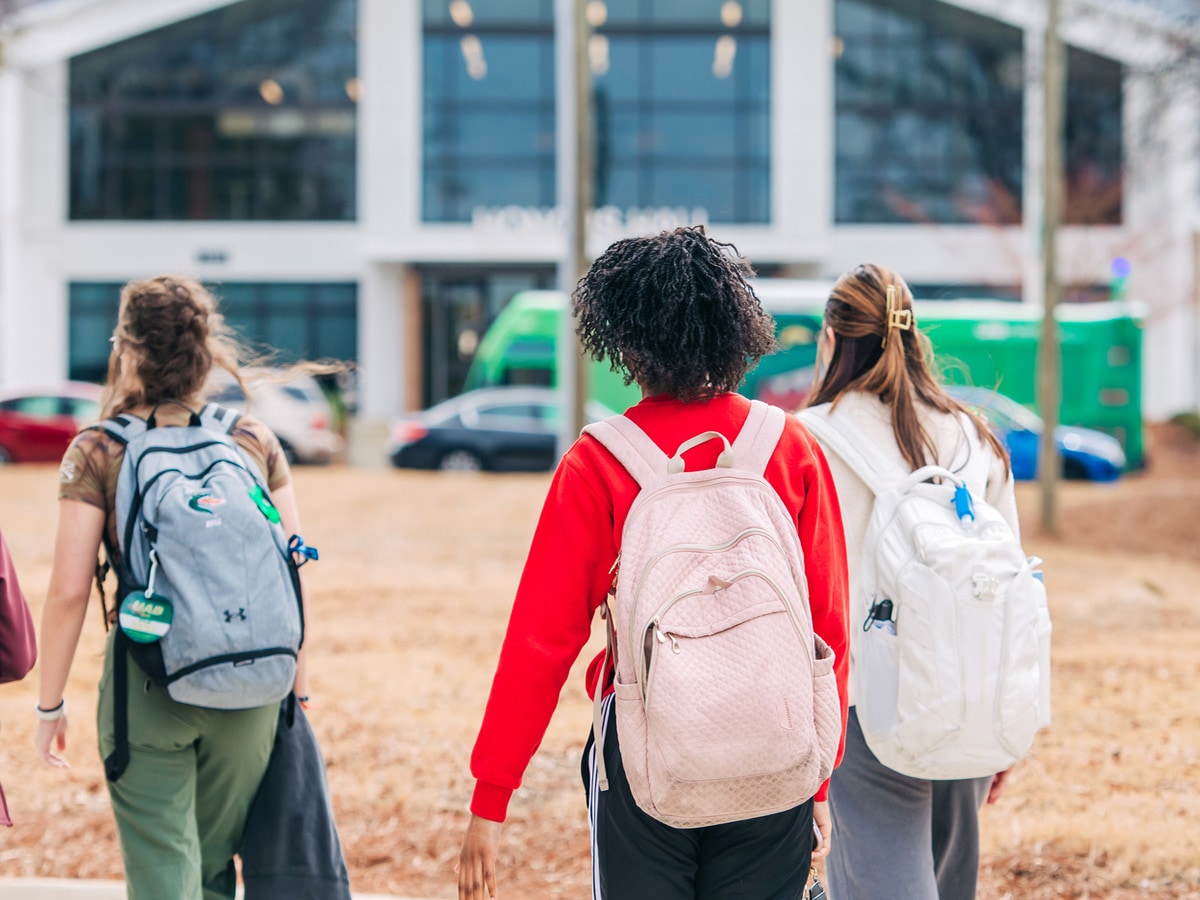 Female students wearing backpacks walking on sidewalk near Honors Hall