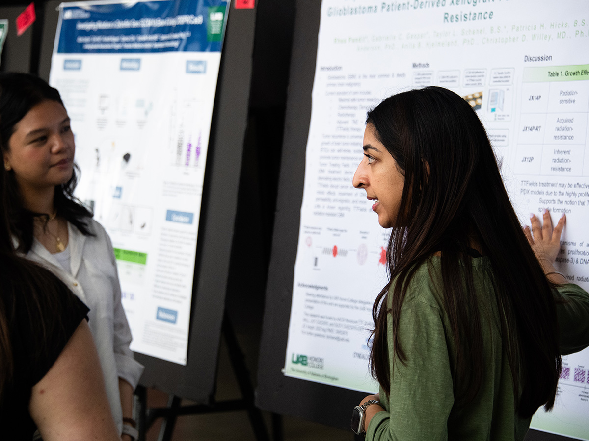 From side, student is speaking with others during her poster presentation at Bartow Arena.