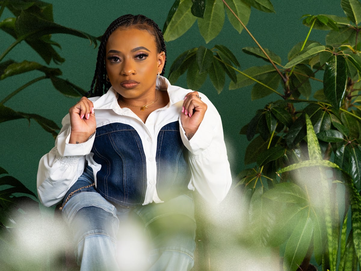 Model Karneshia Patton wears a white and denim outfit with flowers and plants in the background. 