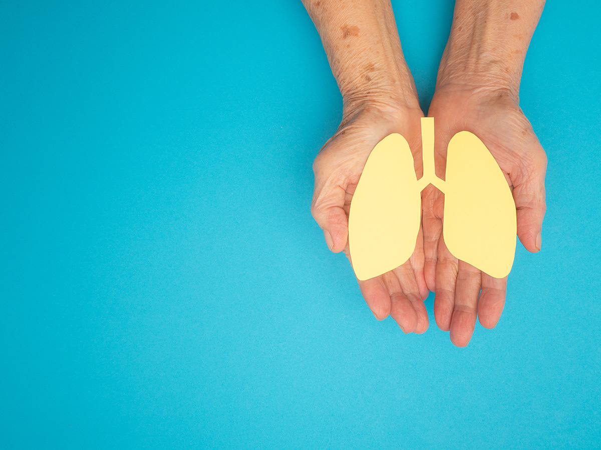 Hands hold yellow paper cut-out of lungs with an aqua blue background.