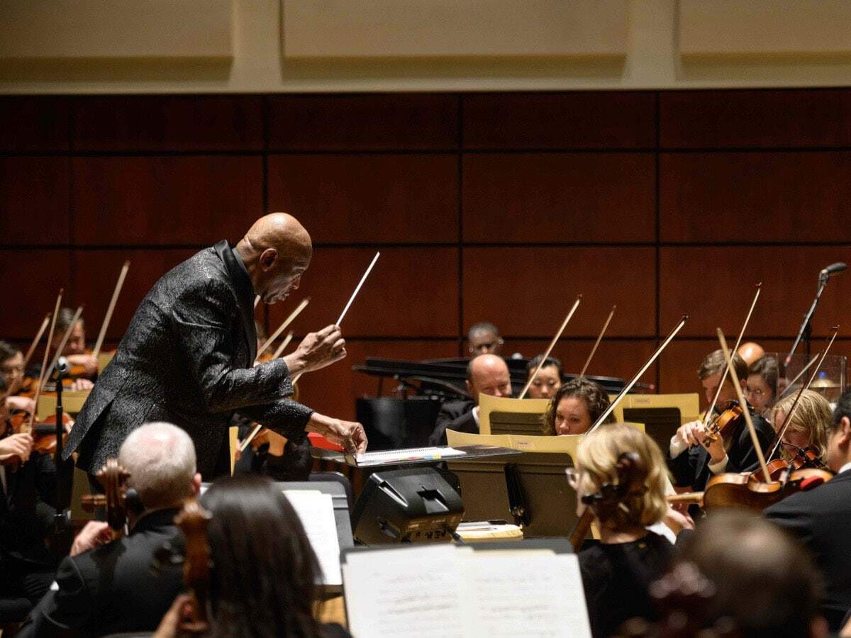 A man stands and conducts an orchestra  of musicians.