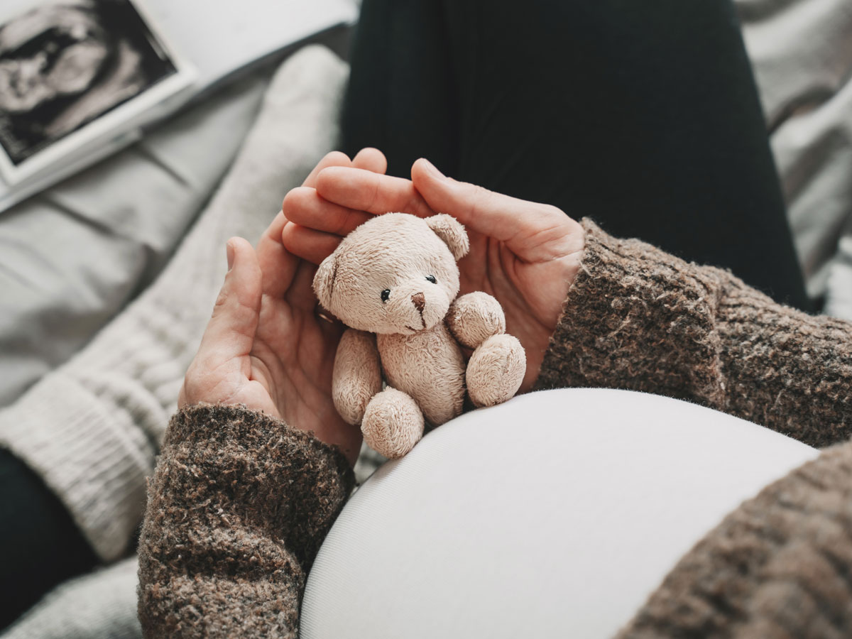  A pregnant woman rests a small teddy bear on her stomach. 