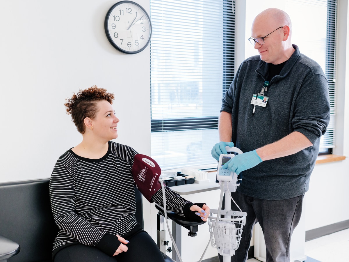 Woman in a chair receiving a blood pressure test by a medical professional.