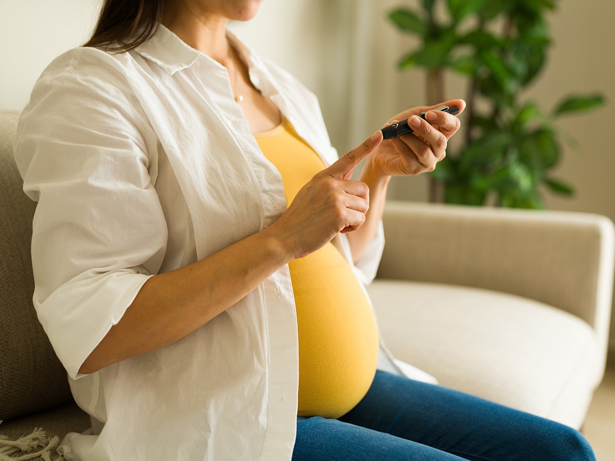 Pregnant woman at home on couch using a diabetes monitor at home.