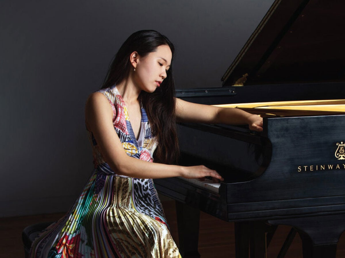  woman in a colorful silk dress sits at a piano looking down at the keys.