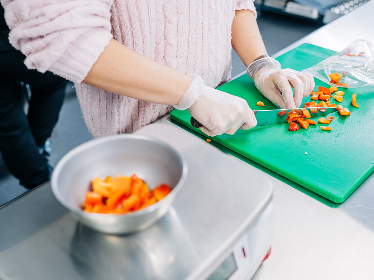 Close up photo of a chef's gloved hands cutting fruit on green cutting board.