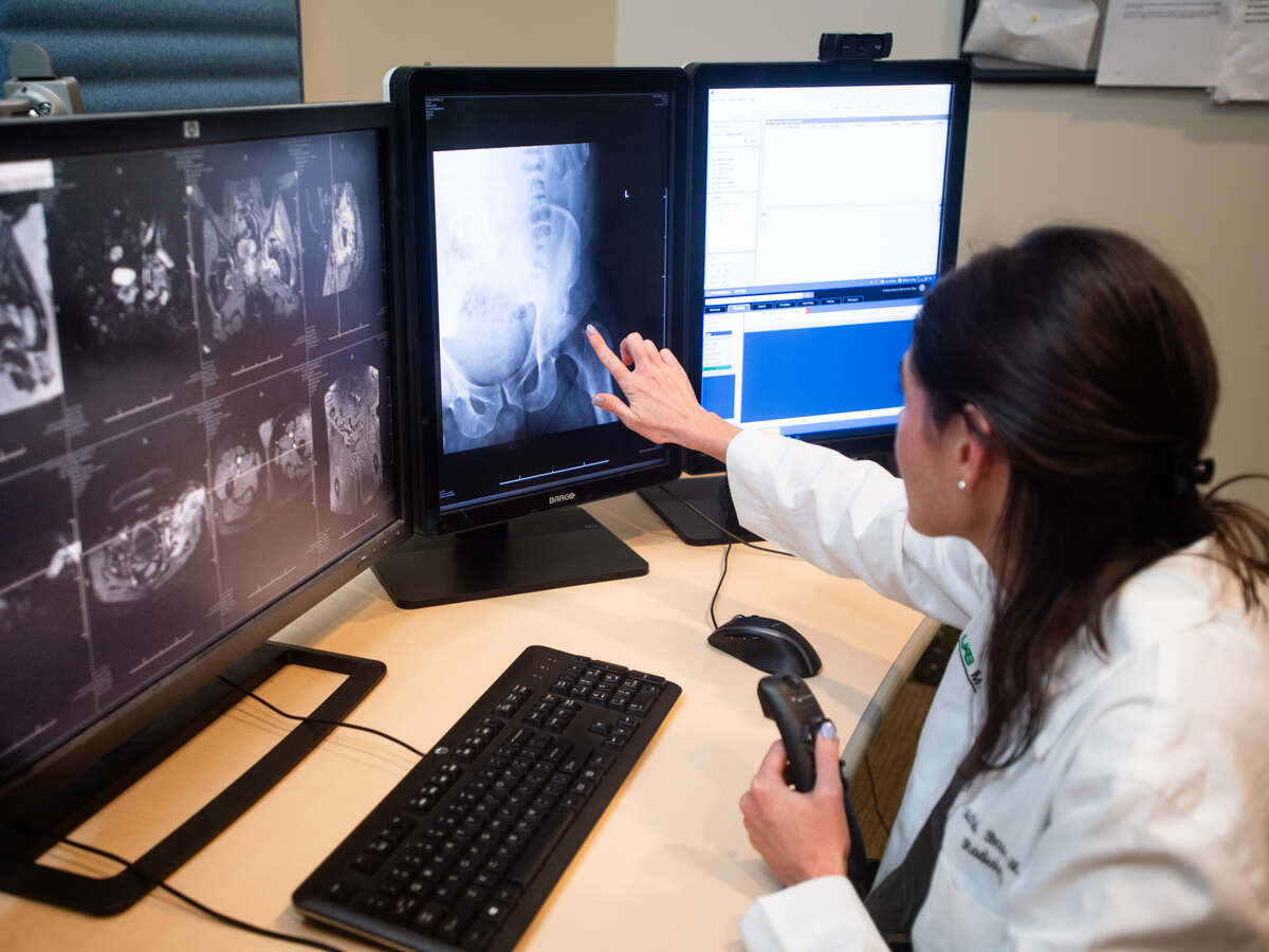 Radiology Reading Room, Wallace Tumor Institute. From side, Dr. Rachel Bass, MD (Assistant Professor, Radiology) is wearing white medical coat and reading x-ray on computer.