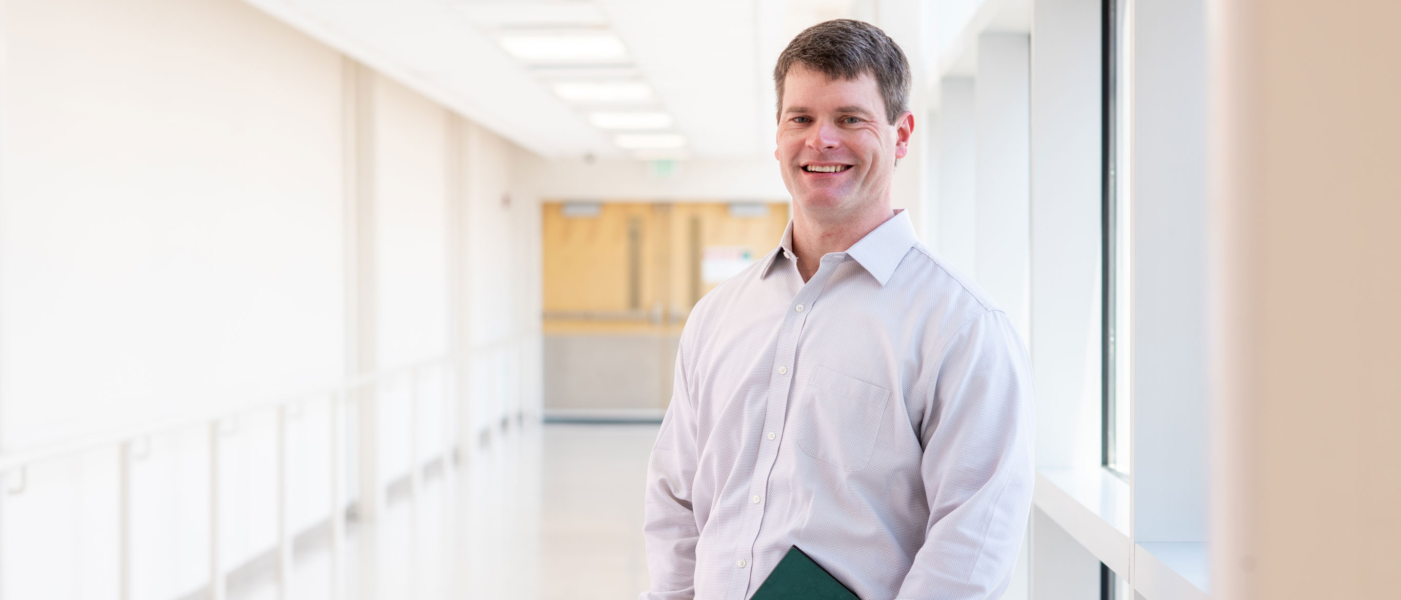 Larry smiling in hallway, holding UAB graduation program