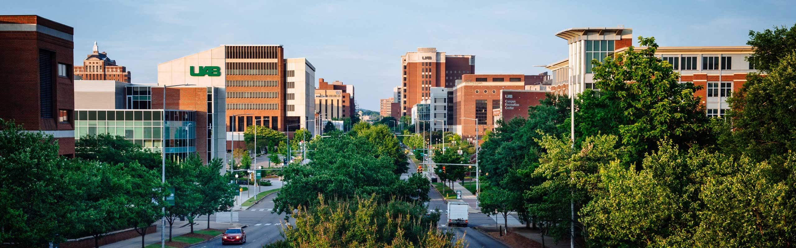 Drone style shot down University Boulevard showing large brick university buildings with UAB logos.