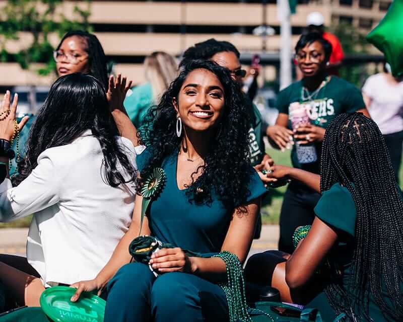 UAB student at a homecoming parade with strings of beads to hand out. 
