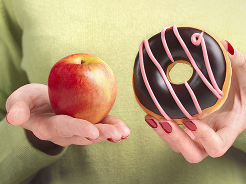 A close up of a woman's hands, one holding an apple the other hand holding a doughnut