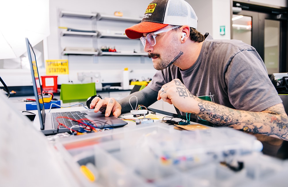 John Riggins looks at a laptop screen as he wires circuits on an arduino board