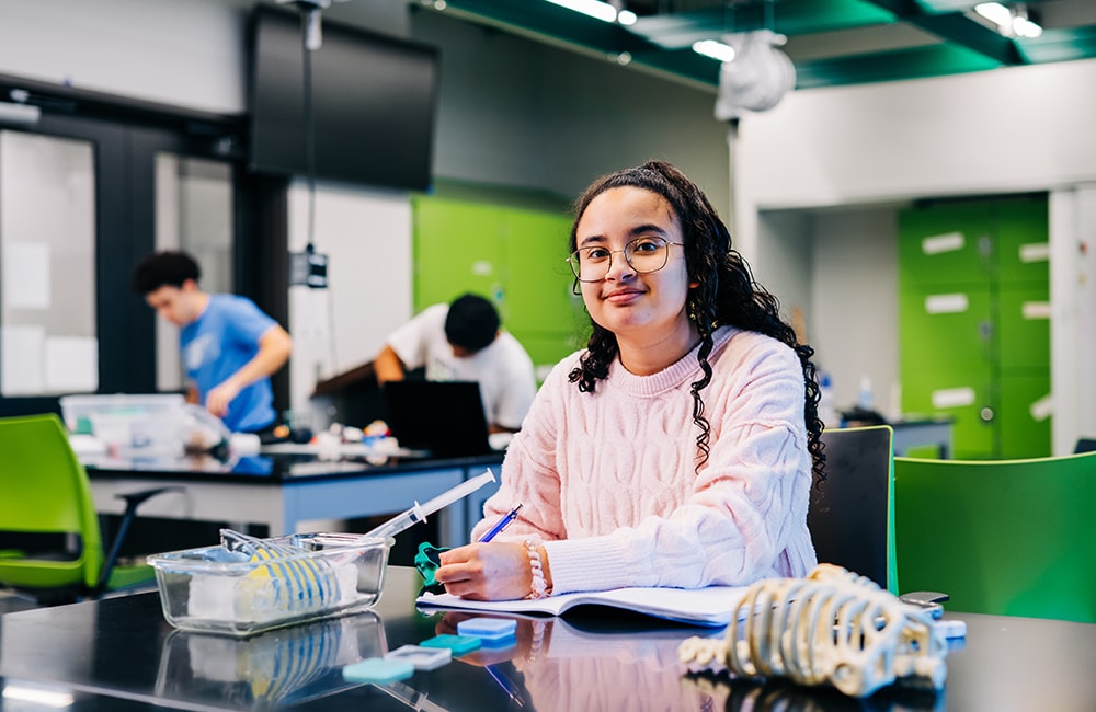 Allie Reinhart sits at a table in the Design x Prototyping Lab with her lab notebook