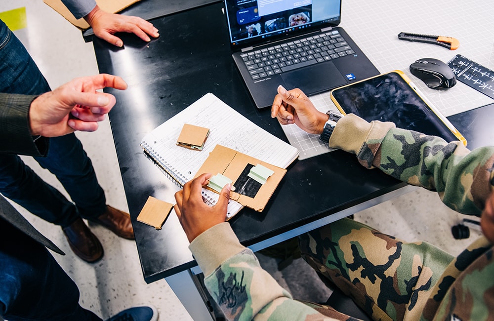 Closeup on desk with cardboard prototype as student Brianna Savage demonstrates her wheelchair ramp concept to Dr. Tim Wick