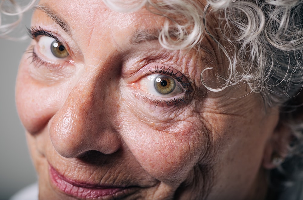 A woman smiles and looks into the camera with a focus on her eyes and irises and curly hair visible framing her face