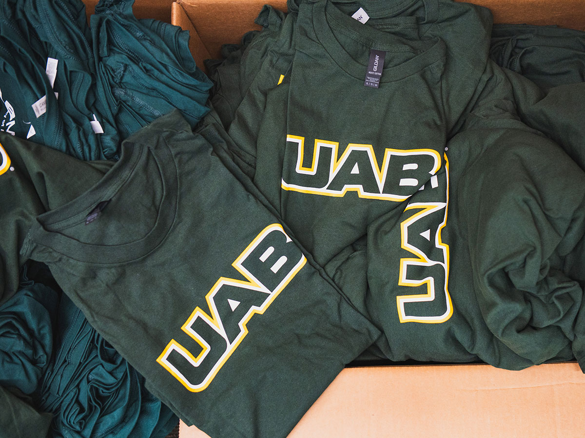 U A B branded T shirts in a cardboard shipping box