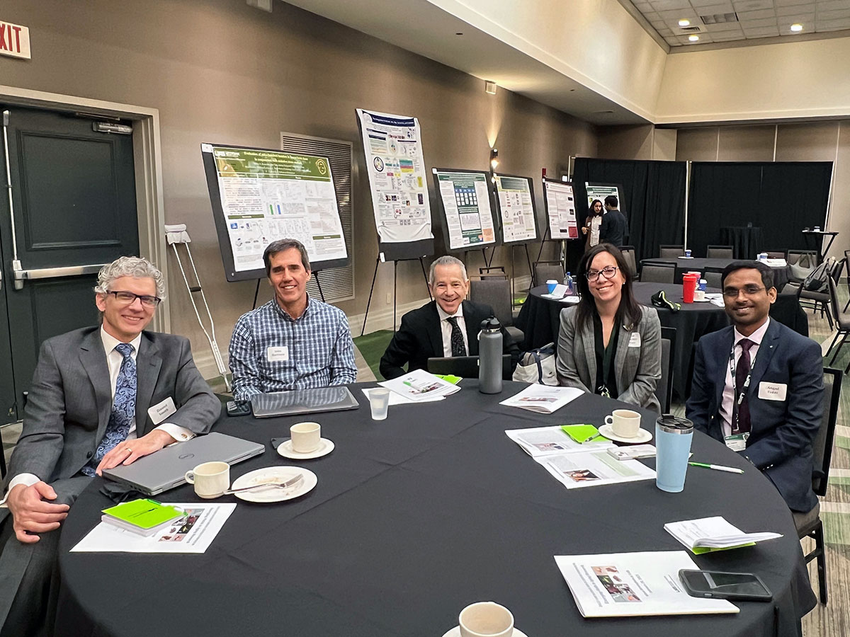 Multiple attendees around a table, poster presentations in the background.