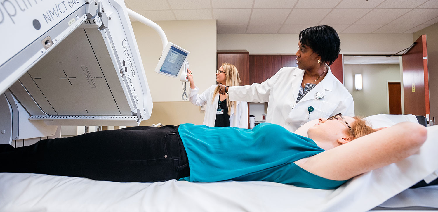 Patient being x-rayed while people in labcoats look at a small screen.