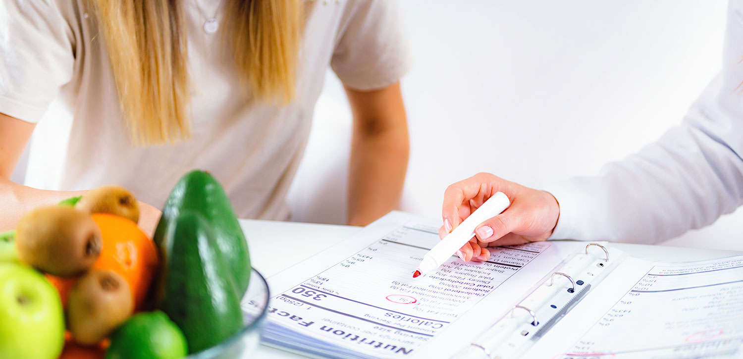 Two people looking at nutrition facts booklet with bowl of fruit in the foreground.