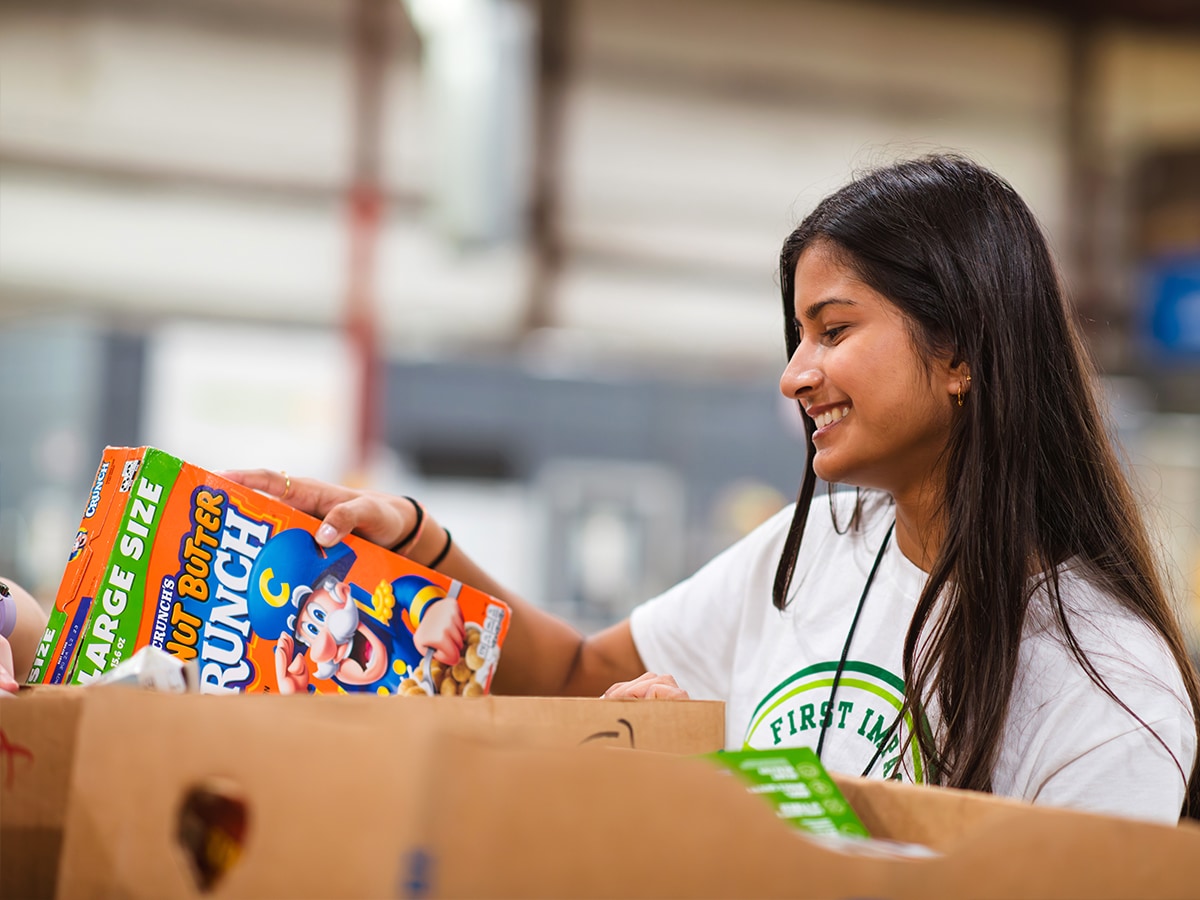 A student volunteers puts a box of Captain Crunch into a box at a food pantry