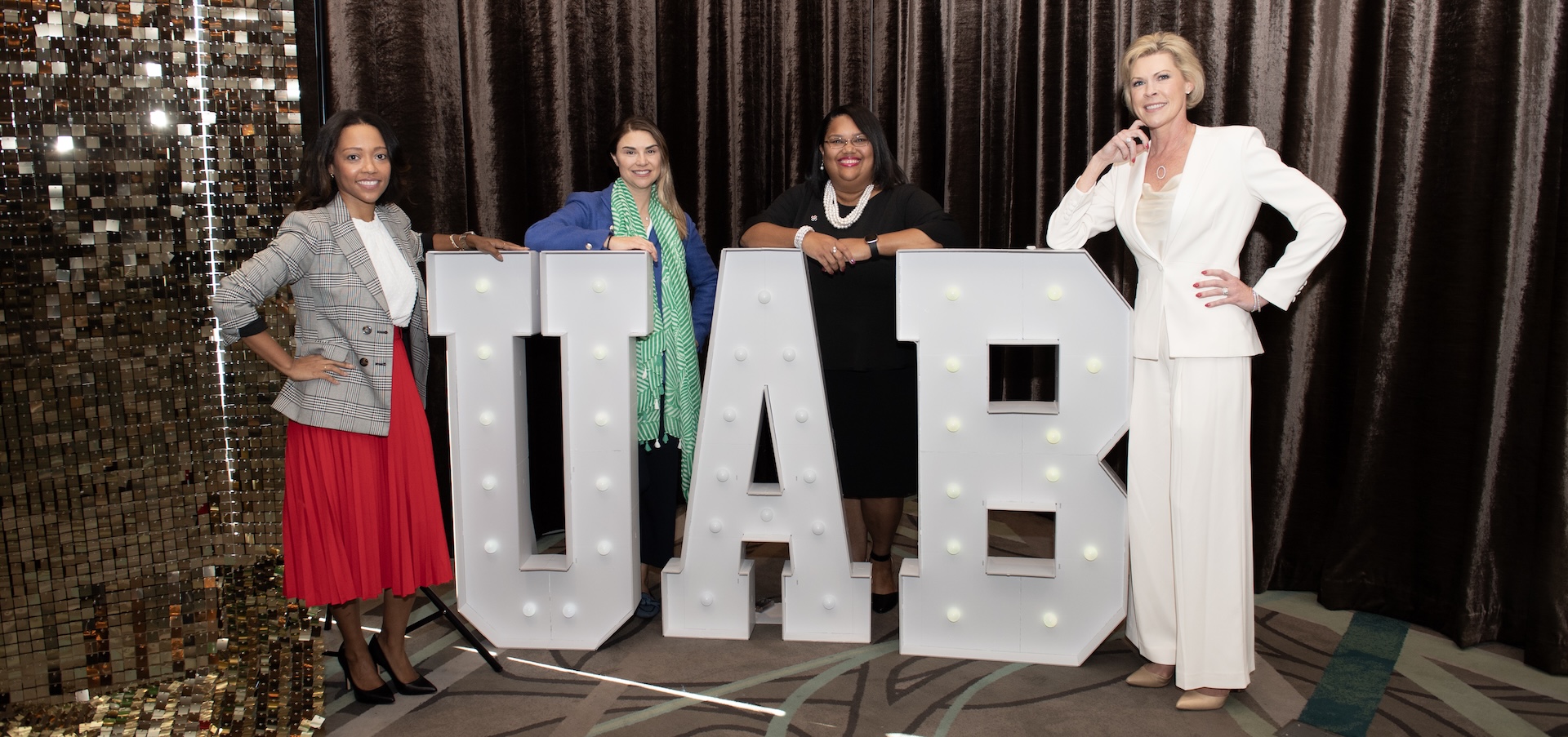 4 professional women standing aside and behind giant UAB light up letters