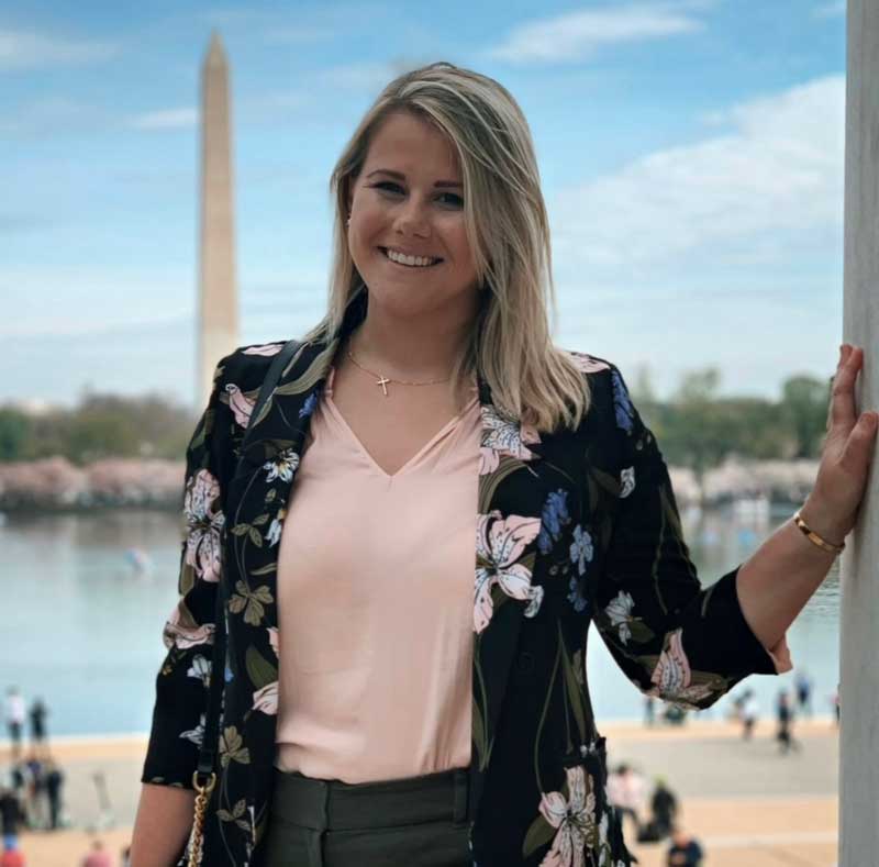 Dr. Caro Wolfner in a pink shirt and black floral jacket, the Washington Monument in the background. 