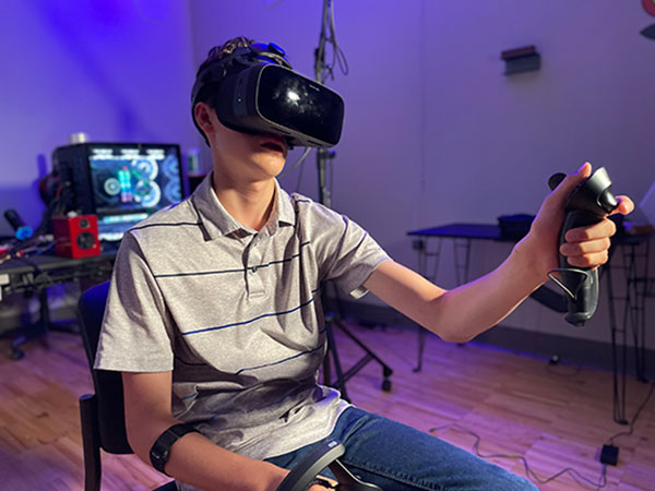 Male user of XR technology wearing a VR headset and holding a controller. 