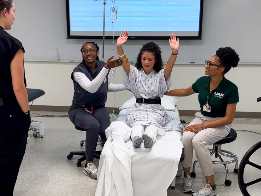 OT and PT students participate in a patient-care simulation, with a first-year student acting as a patient and second-year students providing support during a mobility exercise.