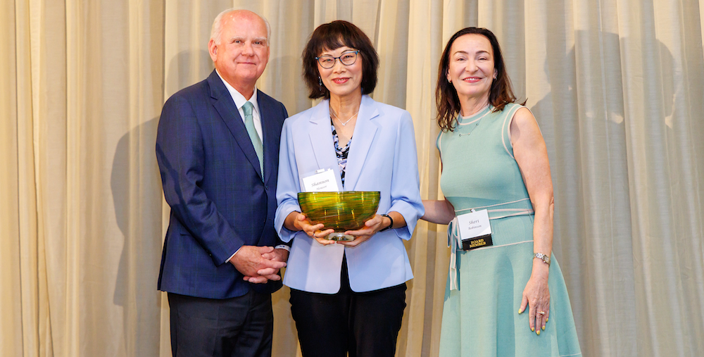 Shannon Houser wearing a lavender jacket, holds her award with UAB President Watts on her right and NAS President Shari Robinson on her left.