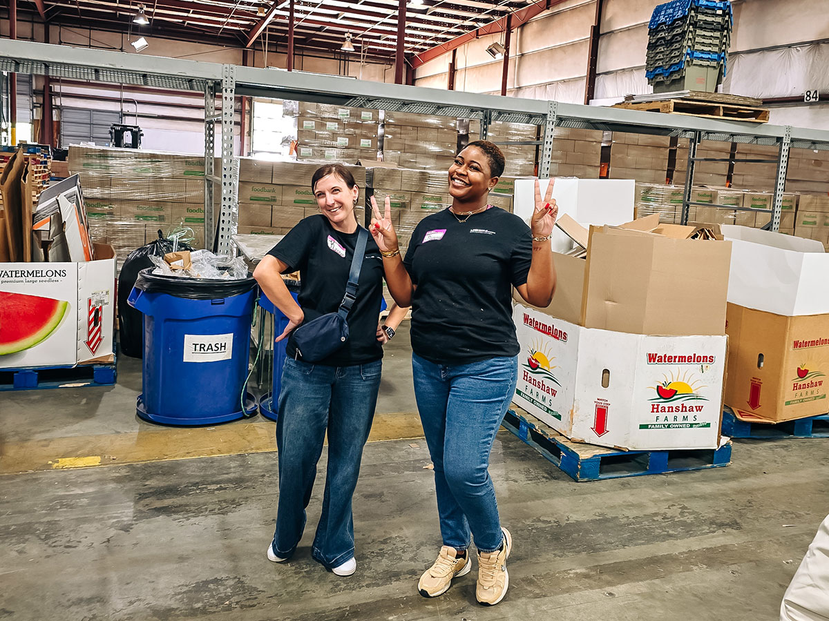 Washington and another woman inside a large warehouse. Washington is smiling and flashing peace signs.